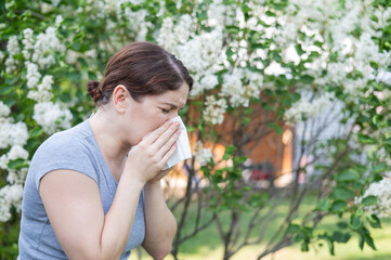 Fototapeta premium Caucasian woman suffers from allergies and blows her nose into a napkin while walking in the park. 