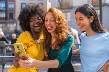 Three multiracial young women on the street taking a selfie in the city, outdoors, friendship, feminist and technology concept