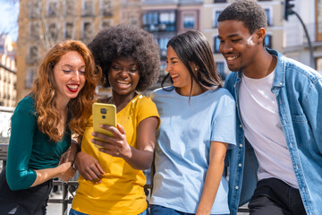 Happy multiethnic friends having fun making a group selfie on the city street, laughing together outdoors