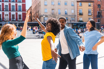 Multi ethnic young friends dancing in a city square, having a good time together in the city