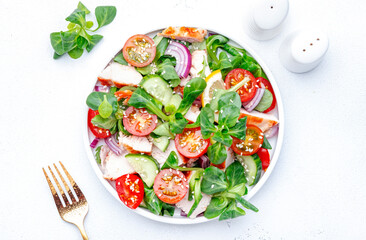 Fresh salad with grilled chicken slice with red tomato, cucumber, red onion, lamb lettuce and sesame seeds on white table background, top view