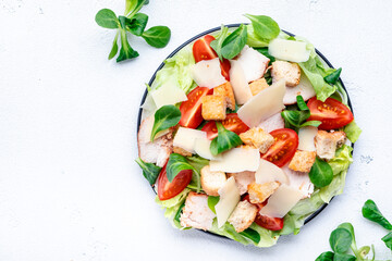 Caesar salad with chicken, iceberg salad, croutons, parmesan cheese and tomatoes with caesar dressing. White table background, top view