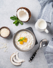 Rice porridge with coconut milk and mango slices in bowl on a blue background. Concept of a nutritious and satisfying food.