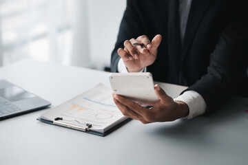 Obraz premium A businessman is using a white calculator to calculate financial numbers, he is sitting in his private office, the businessman examines the financial data from the corporate finance chart.