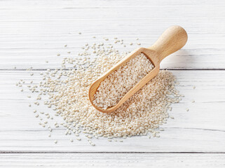 Dry sesame seeds in wooden scoop on white wooden background