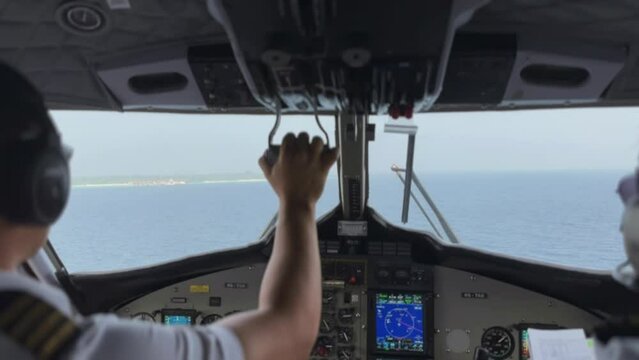 Pilots in the cockpit of a sea plane landing near an island.