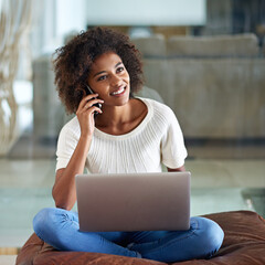 Chatting up a storm. A young woman talking on her cellphone while sitting with her laptop at home.