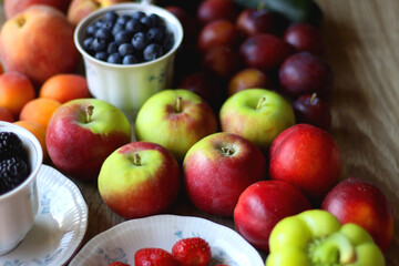 Berries in vintage porcelain dishes, other healthy fruit and vegetable on wooden table. Selective focus.