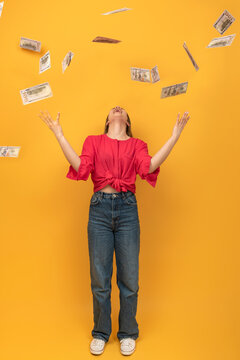 Happy Laughing Woman Tossing Up Dollar Bills While Standing Against Orange Background. Abundance And Waste Of Money. Vertical Frame.