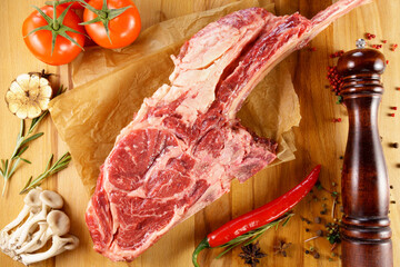 Raw Tomahawk steak on wooden background with spices. Cooking meat