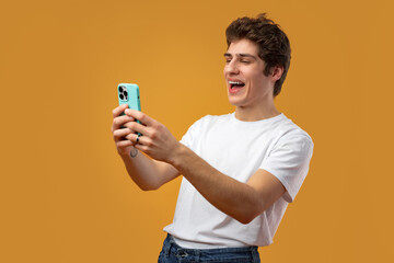 Young happy man looking at his phone against yellow background