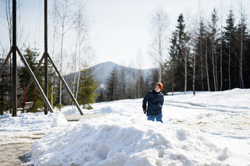 Boy play with snow near big wooden swing in forest of mountains.