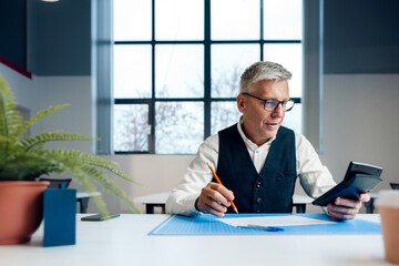Fototapeta na wymiar Busy senior man sitting at office desk with papers and making notes