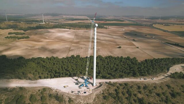 Aerial view of a wind turbine with a group of engineers installing a nacelle in a wind farm under construction. Team of professional with a giant crane lifting a nacelle. Renewable, Spain