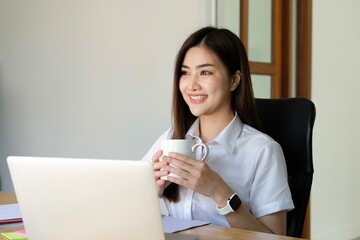 Beautiful young woman working on laptop computer while sitting in cafe. Freelancer business woman thinking about new ideas during work on laptop computer, drink coffee, enjoy of coffee smell.