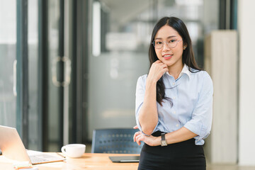 A modern office setting features a businesswoman standing and facing the camera in a portrait shot.