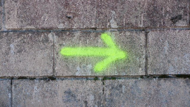 Flecha pintada con spray amarillo fluor en pared de bloques de hormig&oacute;n