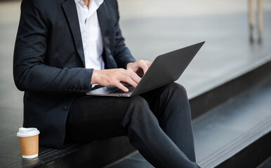 Businesswoman s hands typing on smartphone and  laptop keyboard in morning light computer, typing, online in outside office.