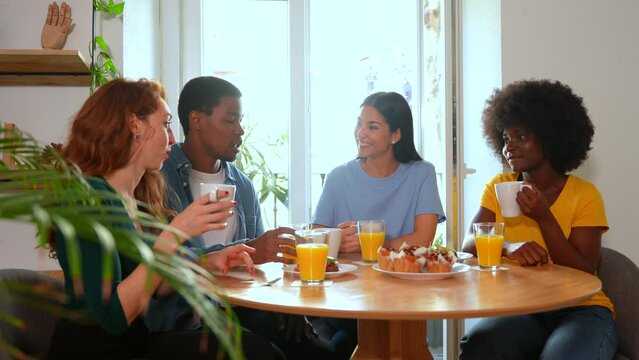Smiling multiethnic friends over breakfast with orange juice and muffins at home