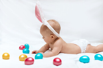 Fototapeta na wymiar A newborn baby with bunny ears and colorful Easter eggs on a white background. Newborn baby Easter bunny. Easter egg hunt. 