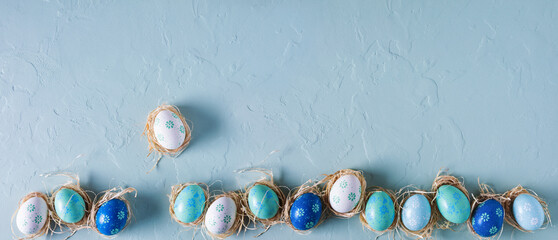Row of hand painted Easter eggs on blue concrete background. Panorama, banner, flat lay, top view...