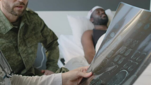 Selective focus shot of unrecognizable military hospital practitioner holding unconscious patients brain X-ray image having conversation with his friend
