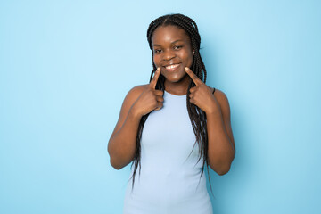 Young african american woman isolated on blue background smiles, pointing fingers at mouth.