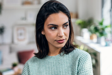 Beautiful young woman looking forwards while standing in the living room at home.