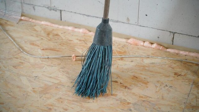 Plastic round broom of blue color at a construction site close-up. Cleaning during renovation. Broom on osb panel