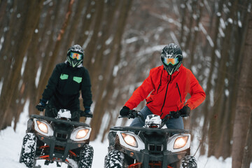Conception of extreme sports. Two people are riding ATV in the winter forest