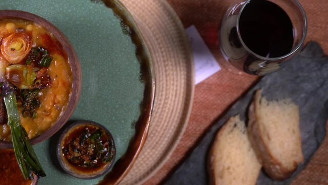 overhead shot of a table with a glass of wine, slices of bread and a turntable with casseroles with homemade food and locro