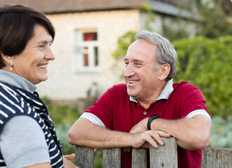 Positive mature man and woman standing near fence in garden