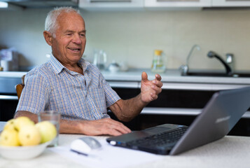 Mature man undergoes online training using aptop and internet while sitting in the kitchen of home