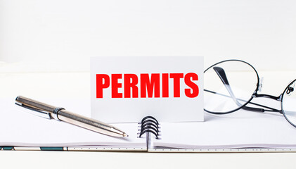Close-up of a white card with the text PERMITS, a stylish pen and glasses on a desktop.
