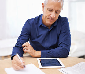 Putting in the extra hours. a mature man using a digital tablet at home.