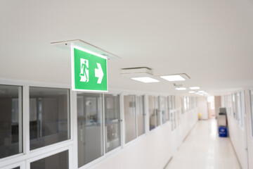 Selective fire exit sign on white ceiling.Green fire escape sign hang on the ceiling in the...