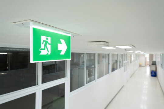 Selective fire exit sign on white ceiling.Green fire escape sign hang on the ceiling in the office.Fire fighting equipment concept.