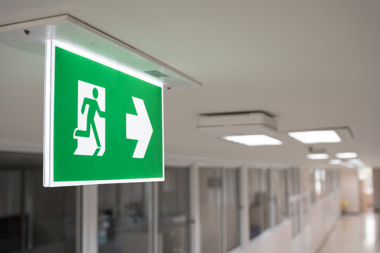 Selective fire exit sign on white ceiling.Green fire escape sign hang on the ceiling in the office.Fire fighting equipment concept.