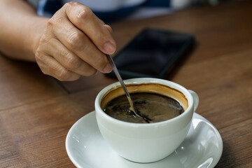 Woman hand and hot coffee in the white cup on wooden table background.Cafe drinking menu black coffee at the restaurant with copy space.