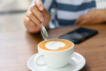 Close up woman hand and white coffee cup with heart shape latte art menu on wooden background in the cafe.