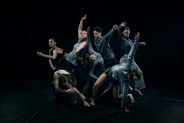 Fototapeta na wymiar Flexibility. Group of young people expressively dancing against black studio background. Concept of modern freestyle dance, contemporary art, movements, hobby and creative lifestyle