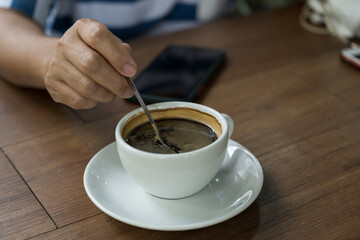 Woman hand and hot coffee in the white cup on wooden table background.Cafe drinking menu black coffee at the restaurant with copy space.