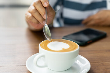 Close up woman hand and white coffee cup with heart shape latte art menu on wooden background in the cafe.