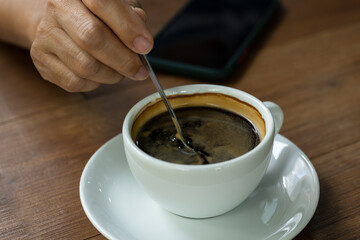 Woman hand and hot coffee in the white cup on wooden table background.Cafe drinking menu black coffee at the restaurant with copy space.