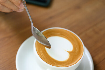 Close up woman hand and white coffee cup with heart shape latte art menu on wooden background in the cafe.