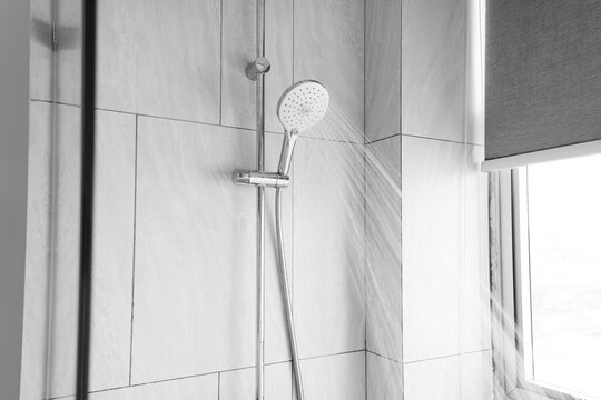 Close up shower head in modern bathroom with water drops flowing.Sanitary ware for bathroom interior.Running water of shower faucet.Fresh shower behind wet glass window with water drops splashing.