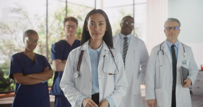 Group of Happy Multiethnic Team of Female and Male Doctors, Nurses and Healthcare Professionals Posing for Camera and Smiling. Portrait of a Confident Asian Physician Standing First in Focus