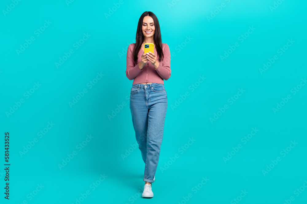 Sticker Full size portrait of cheerful pretty girl walking use smart phone typing isolated on turquoise color background