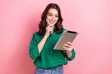 Photo of minded intelligent smart woman with wavy hairdo dressed green shirt look at tablet choose product isolated on pink background