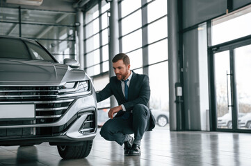 Fototapeta na wymiar Man in suit and tie is sitting and checking quality of the vehicle in the car showroom